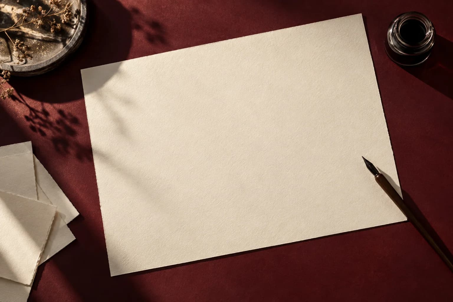 Sunlit paper, ink and a calligraphy pen on a burgundy studio desk